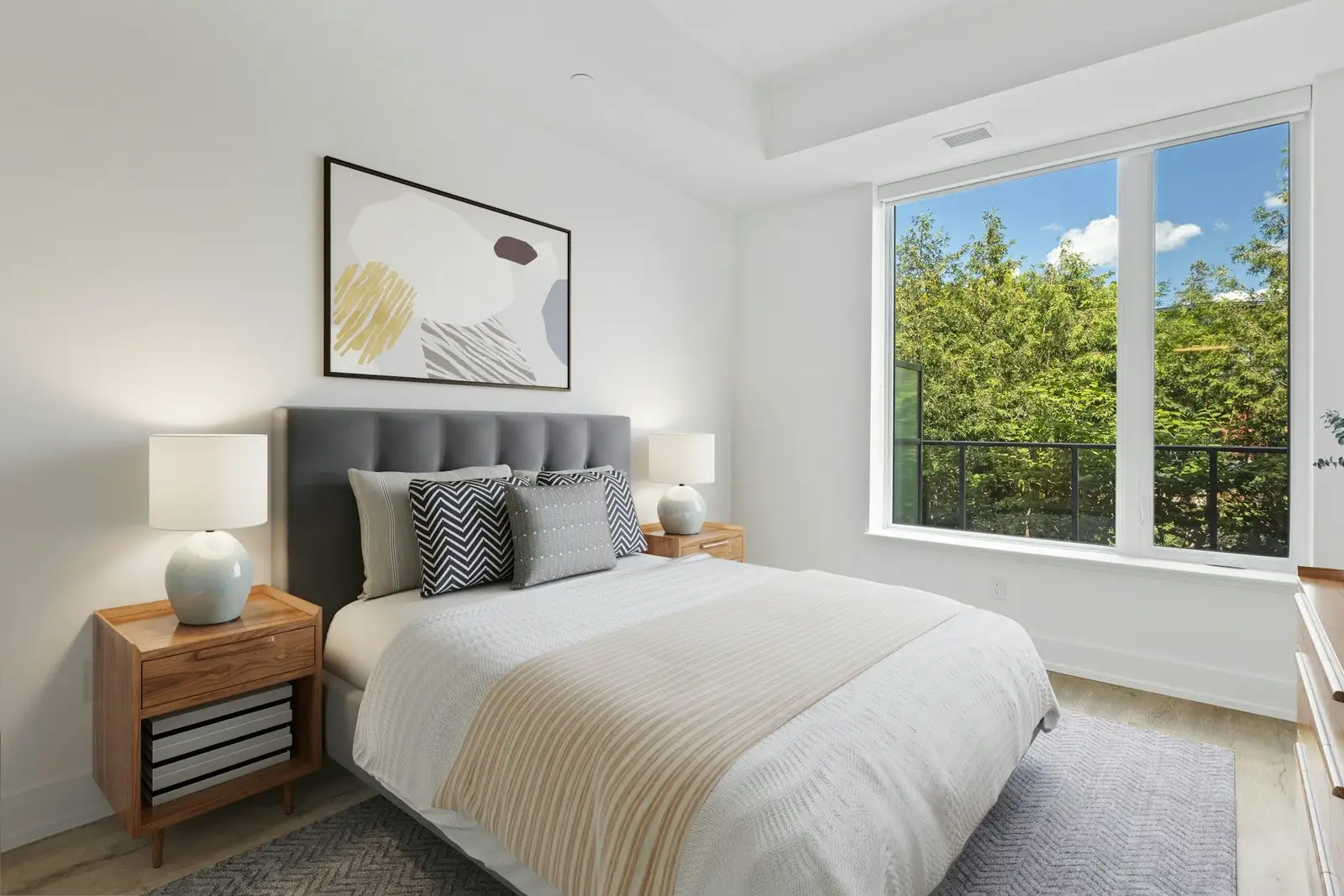 Bedroom with a grey headboard and a large window onto trees