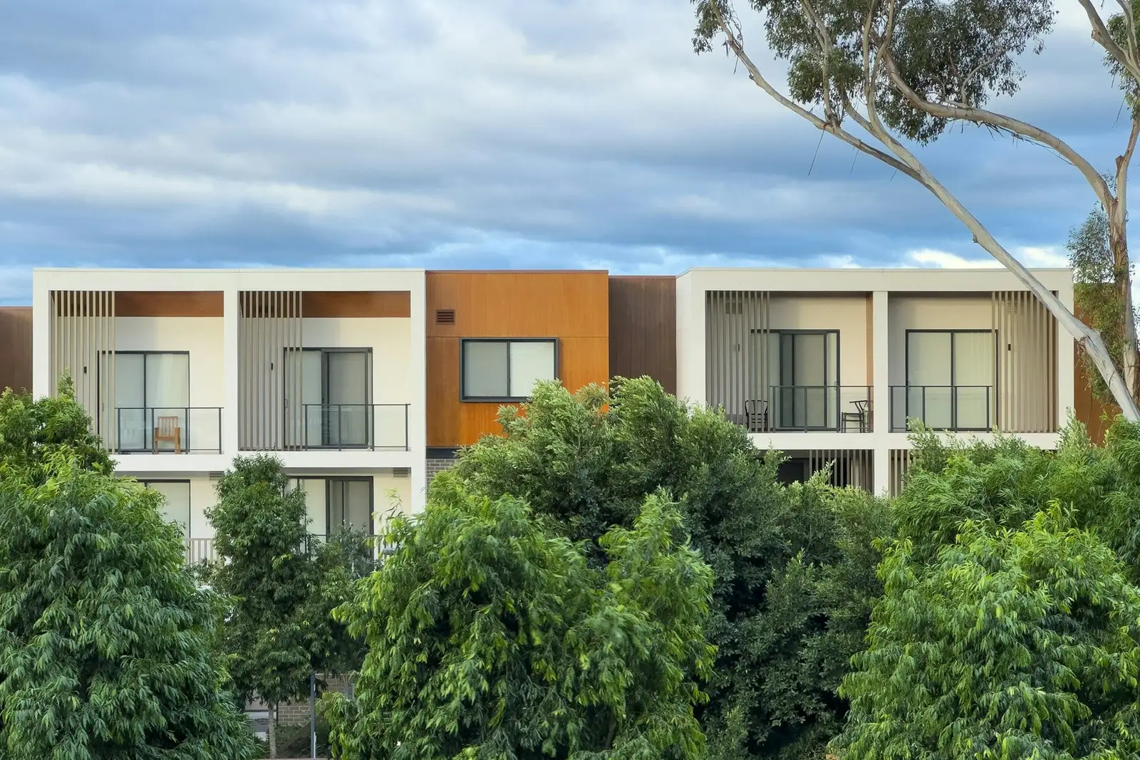 Low-rise apartment building with balconies behind trees