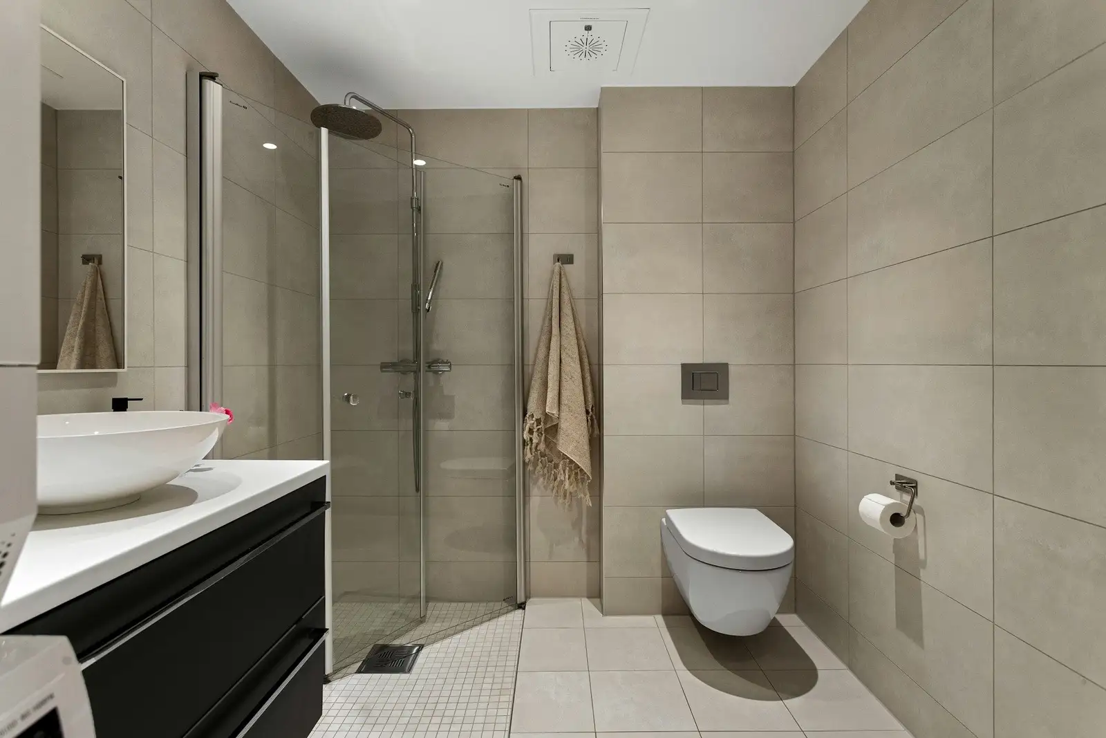 Beige tiled bathroom with a glass shower and a wall-hung toilet