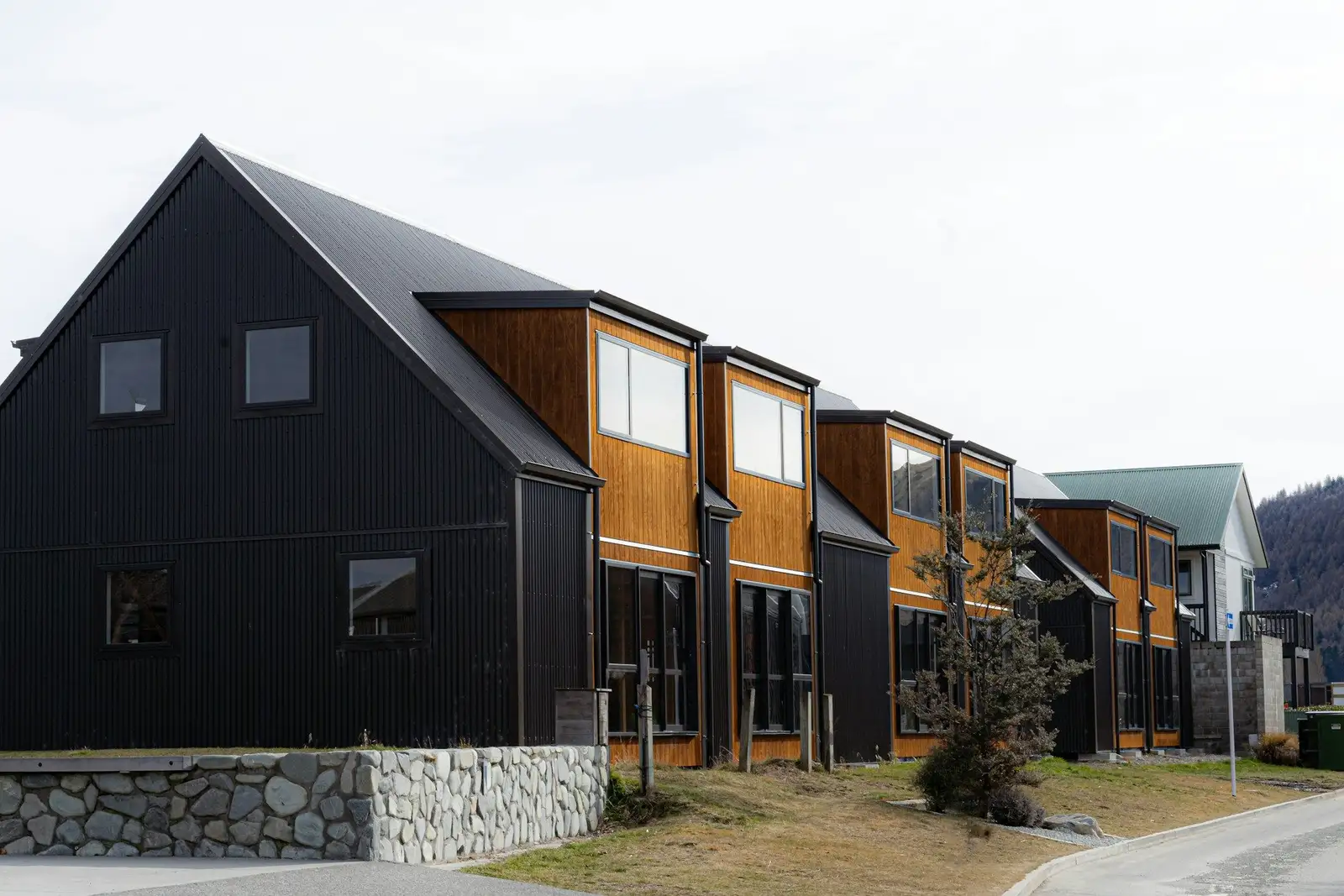 Row of dark-clad townhouses with wood accents above a stone wall