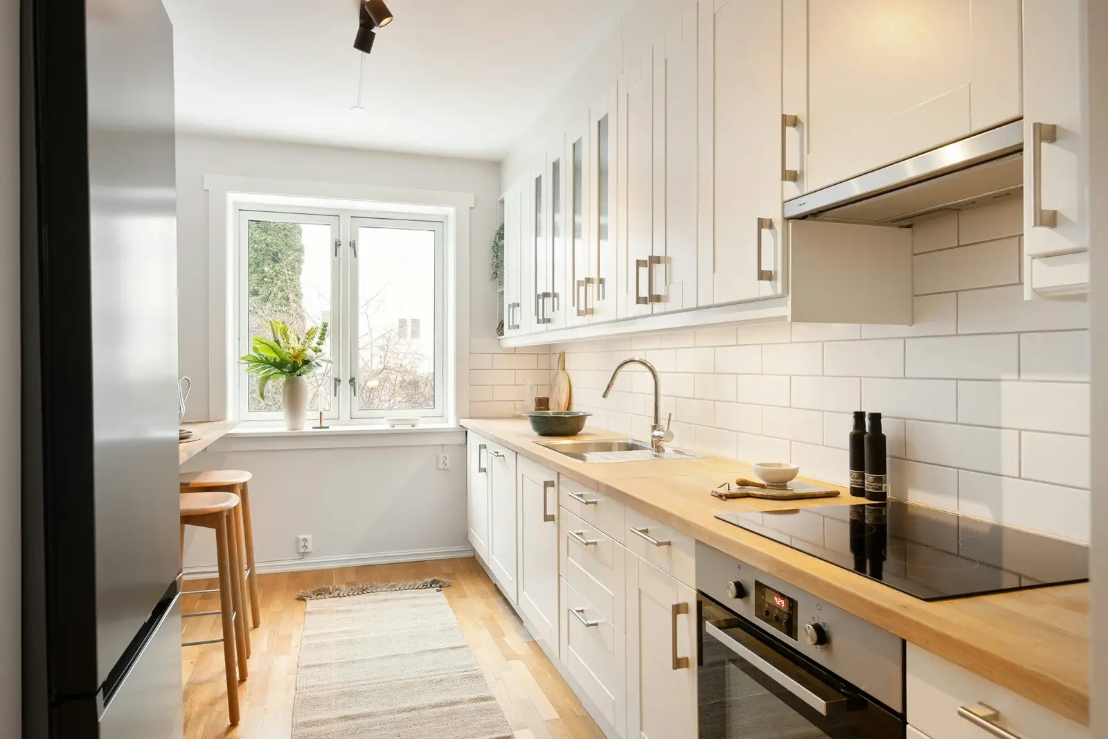 Narrow white kitchen with a wooden counter and a window