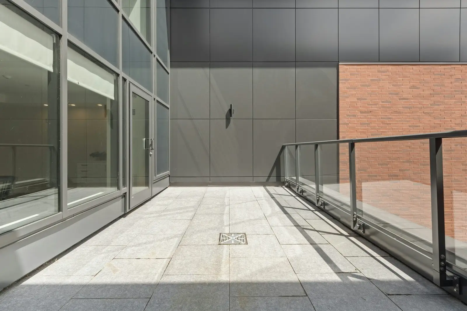 Empty terrace with a glass railing beside a grey wall